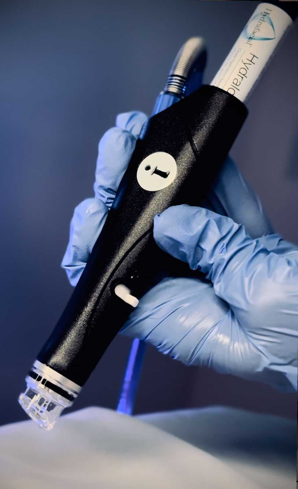 Hand using a hydrafacial device for skincare treatment, wearing blue gloves.