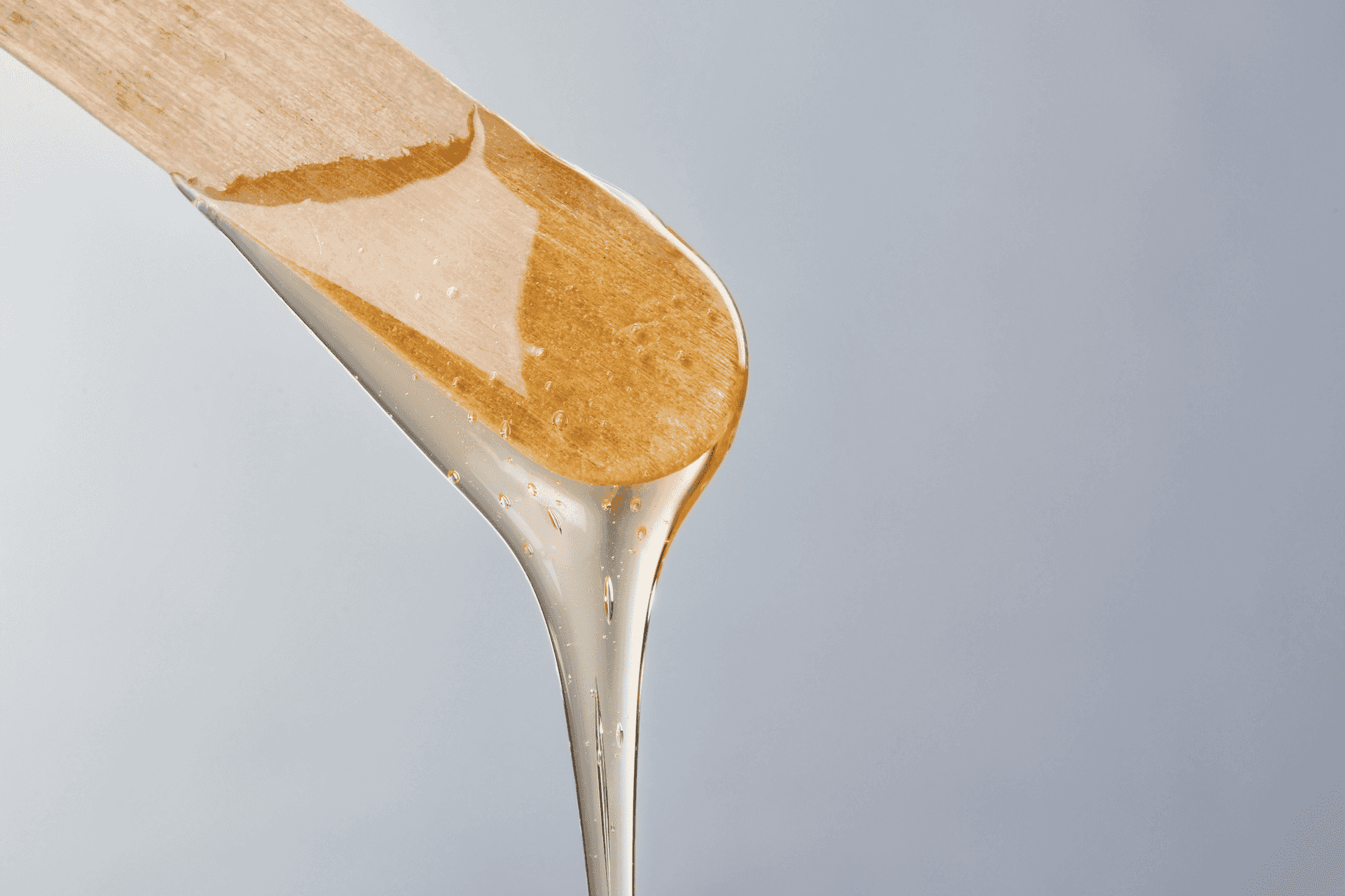 Wooden spatula with dripping golden honey against a light grey background.