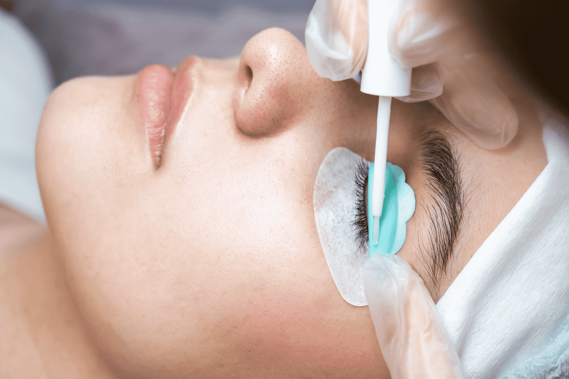 Woman receiving eyelash curling treatment, with protective pads and a professional applying solution.