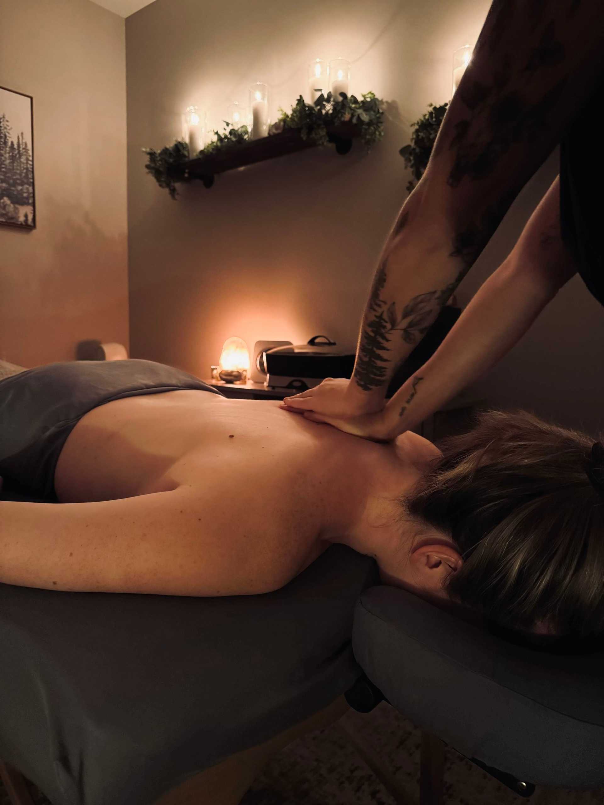 Person receiving a back massage in a dimly lit room with candles and greenery on shelves.