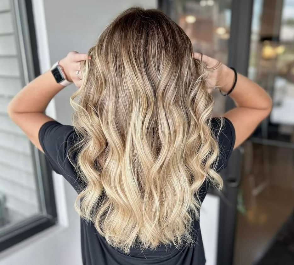 Person with wavy, blonde-highlighted hair viewed from the back, wearing a black shirt.