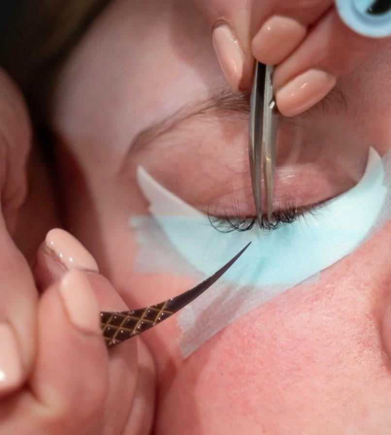 Close-up of a person receiving an eyelash extension treatment with precision tools.