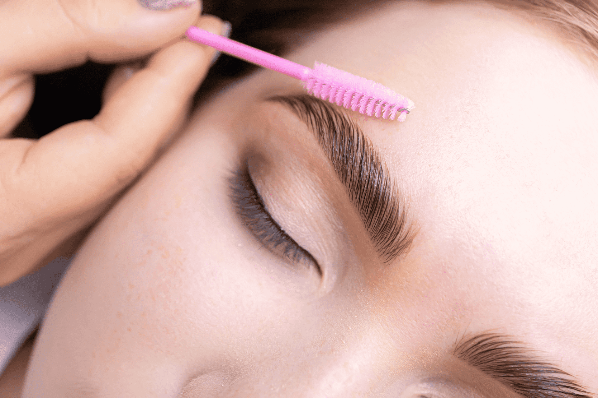 Close-up of a person receiving eyebrow grooming with a pink brush.