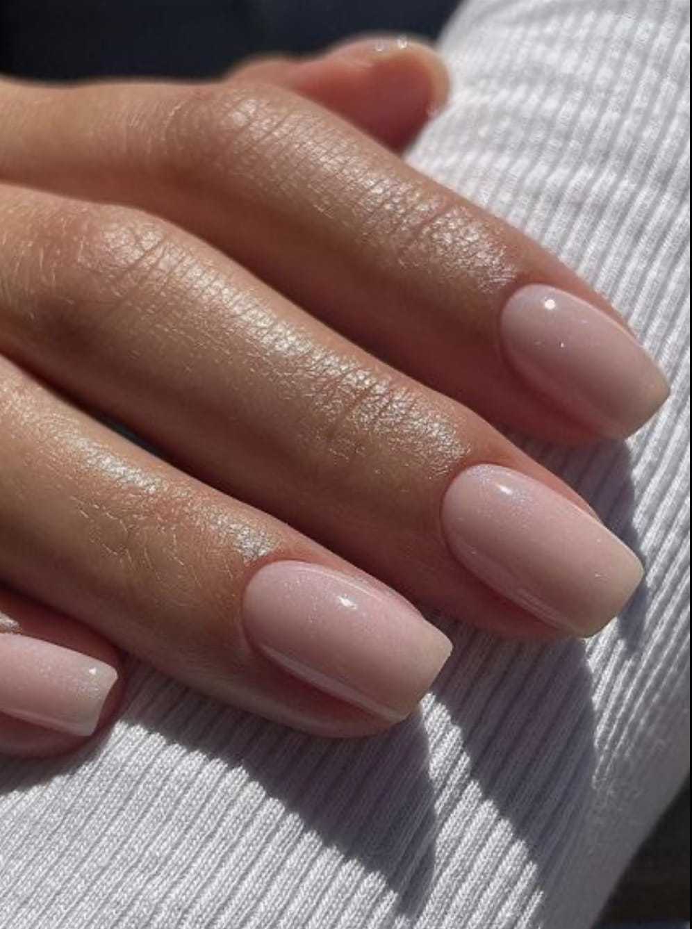 Close-up of a hand with neatly manicured, pale pink nails on a white textured fabric.