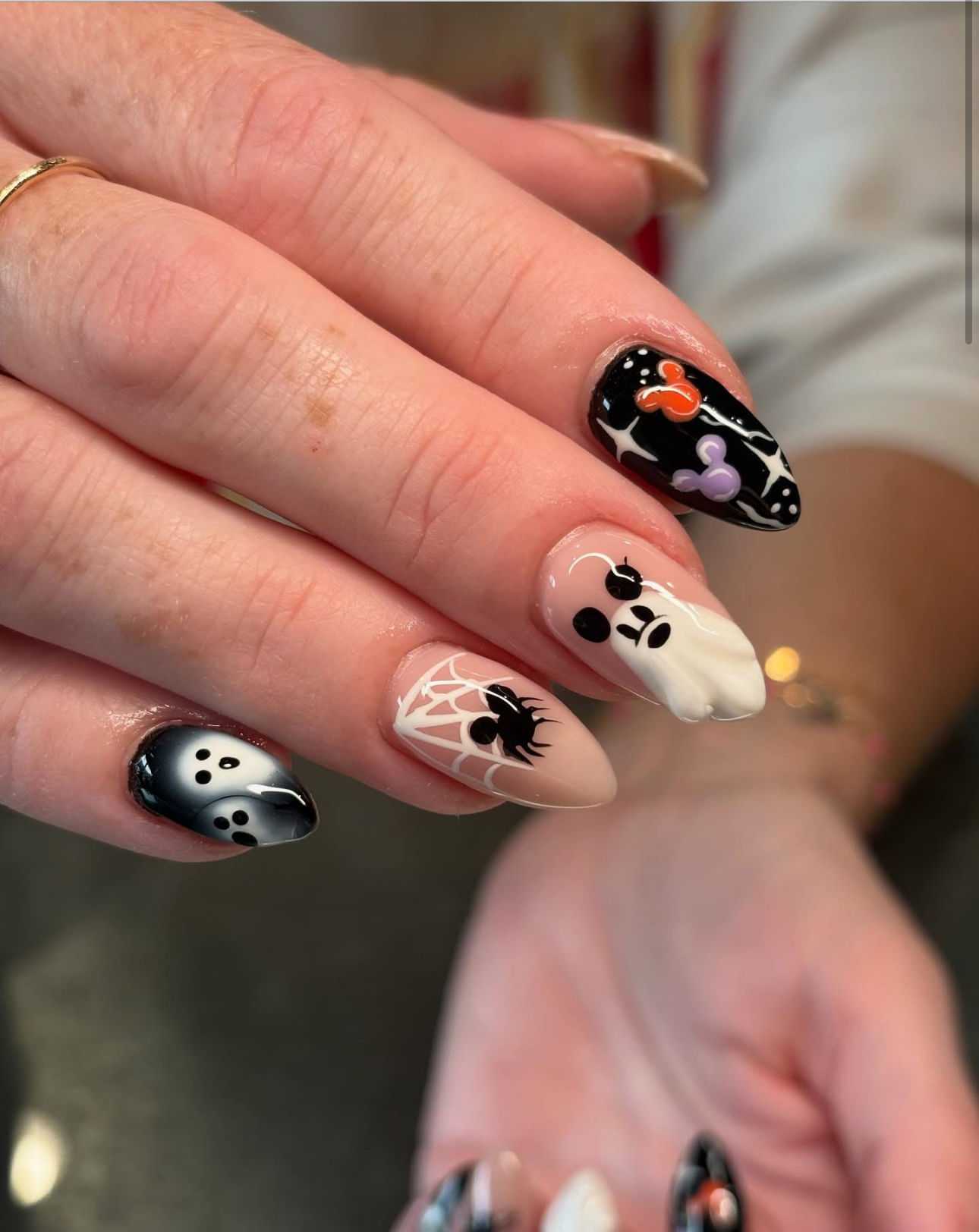 Halloween-themed nail art with spider, ghost, and colorful patterns.