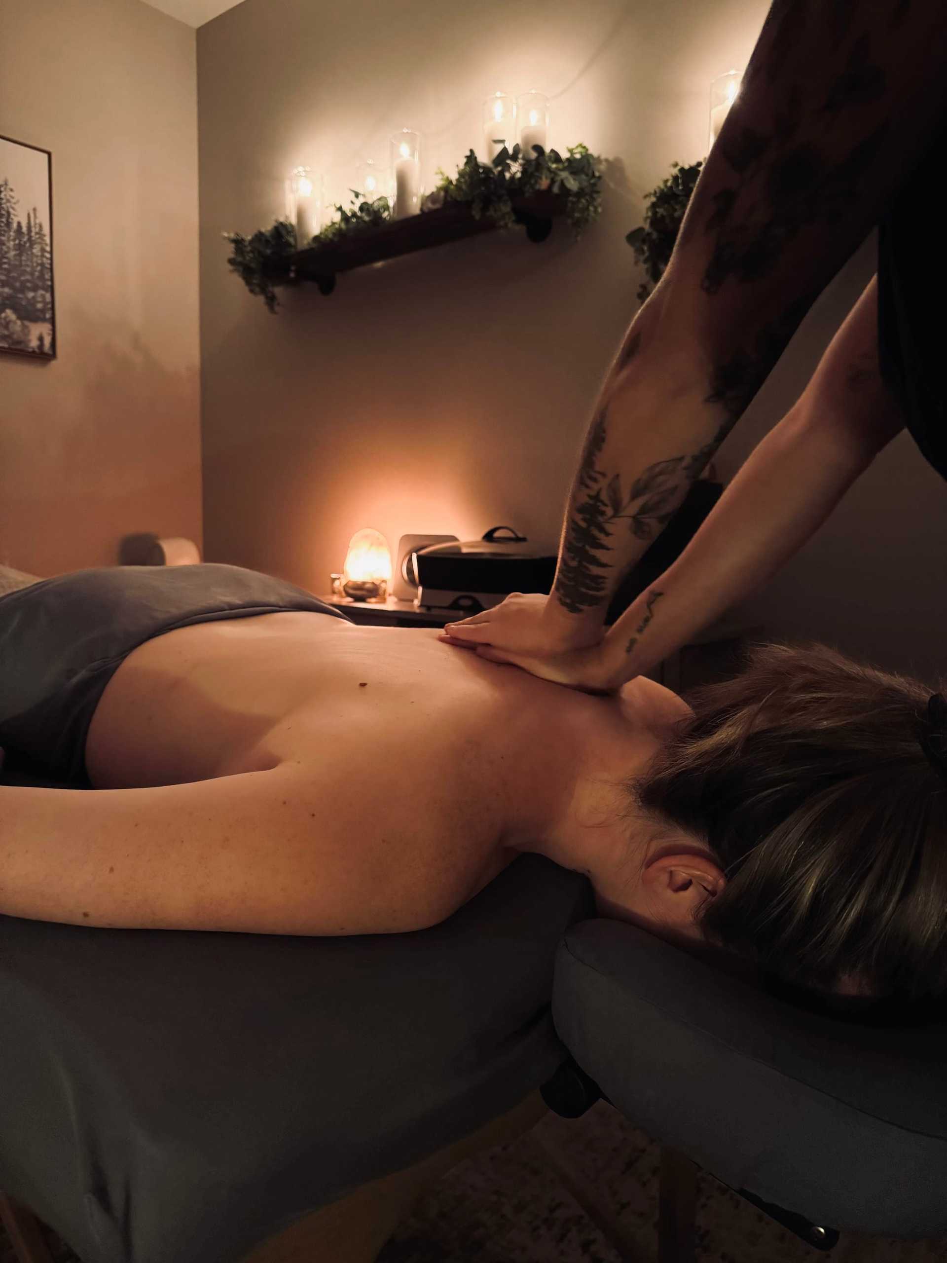 Person receiving a back massage in a dimly lit room with candles and greenery on shelves.