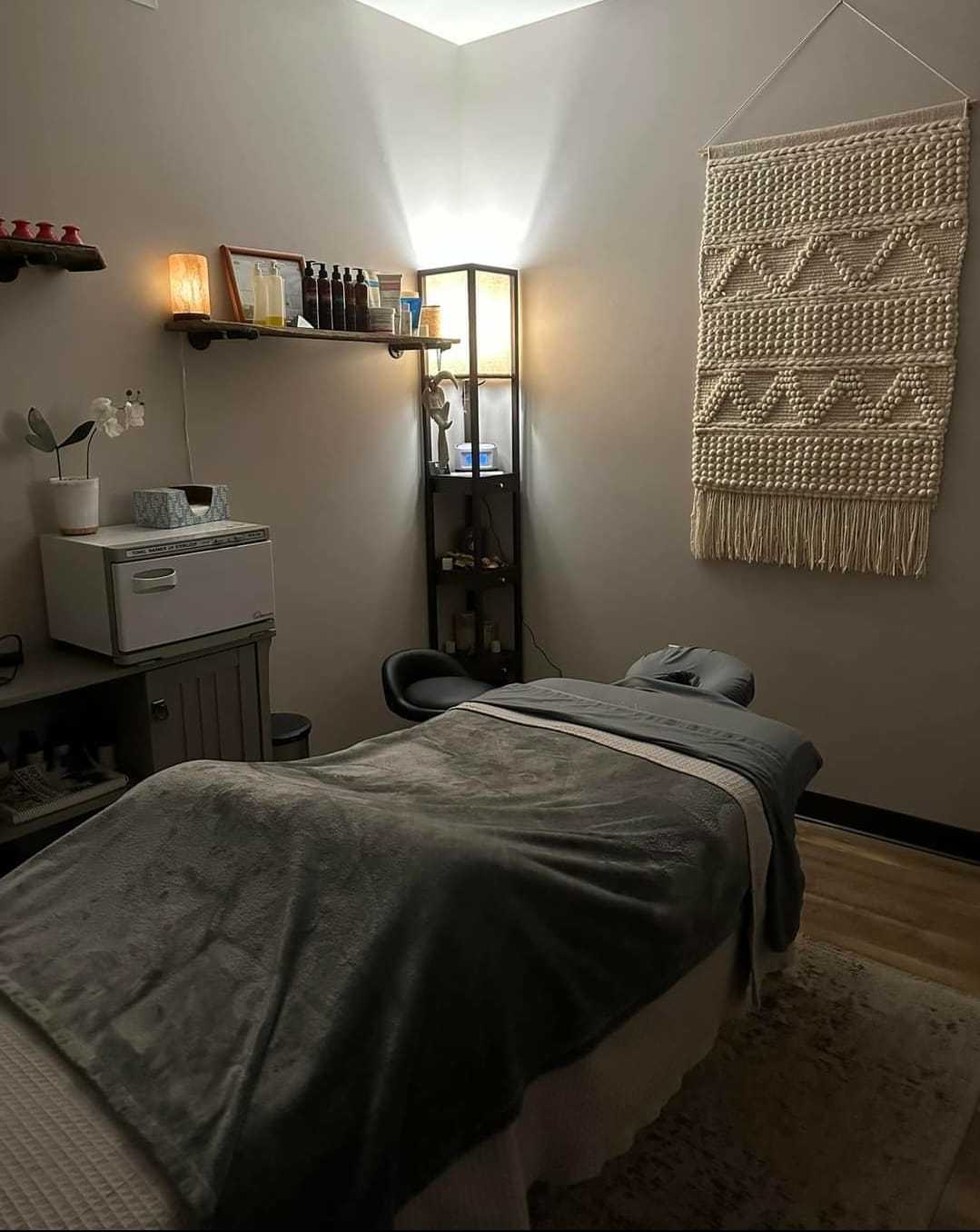 Cozy massage room with a bed, soft lighting, and wall decor.